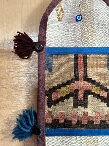 Handmade Turkish wall hanging with vintage rug patterns, featuring colorful tassels, evil eye beads, and geometric designs on a wood panel background. Unique bohemian decor made from authentic Turkish rug fragments, perfect for home styling.