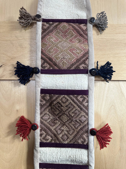 Handmade Turkish wall hanging with vintage rug patterns, featuring colorful tassels, evil eye beads, and geometric designs on a wood panel background. Unique bohemian decor made from authentic Turkish rug fragments, perfect for home styling.