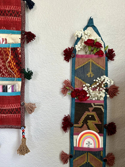 Handmade Turkish wall hanging with vintage rug patterns, featuring colorful tassels, evil eye beads, and geometric designs on a wood panel background. Unique bohemian decor made from authentic Turkish rug fragments, perfect for home styling.