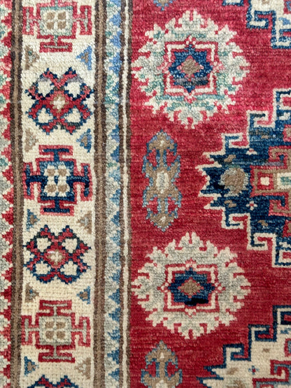 Hand-knotted 2x3 foot mini pile rug featuring a colorful geometric design, large central motif and geometric border - wool material with pops of red, light blue, navy and white. 