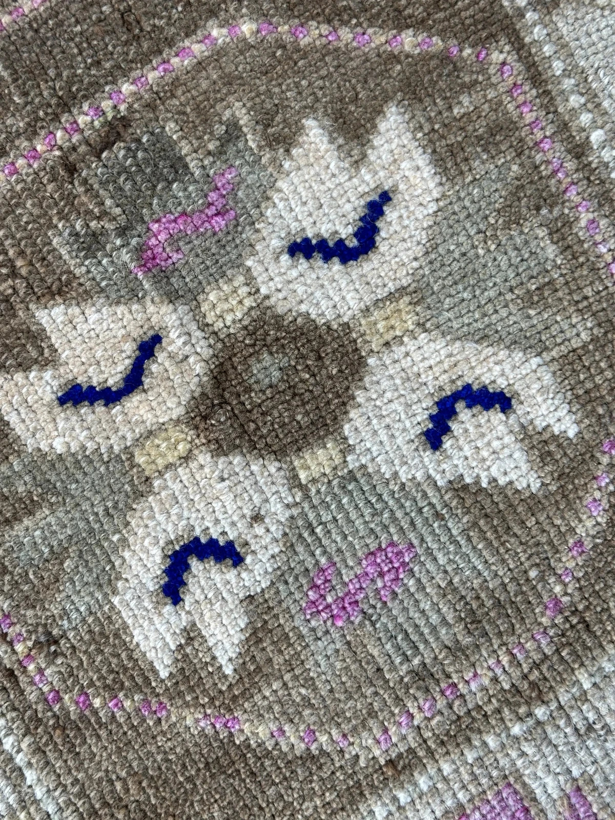 Handmade neutral Turkish mini rug featuring sand, brown and pops of pink and blue with geometric patterns around the border