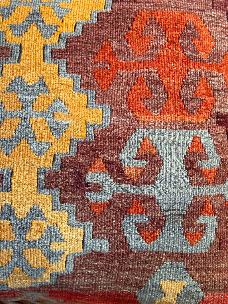 Square vintage Turkish kilim pillow with bold geometric patterns in yellow, orange, and light blue on a deep red wool background, handwoven from repurposed rug fragments.