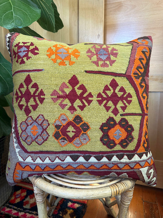 Handwoven kilim pillow crafted from upcycled Turkish rugs, featuring vibrant tribal motifs in olive green, burgundy, orange, and gray tones