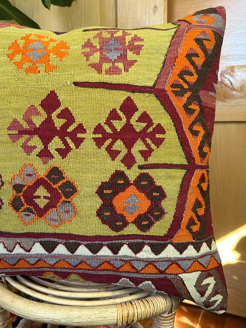 Handwoven kilim pillow crafted from upcycled Turkish rugs, featuring vibrant tribal motifs in olive green, burgundy, orange, and gray tones