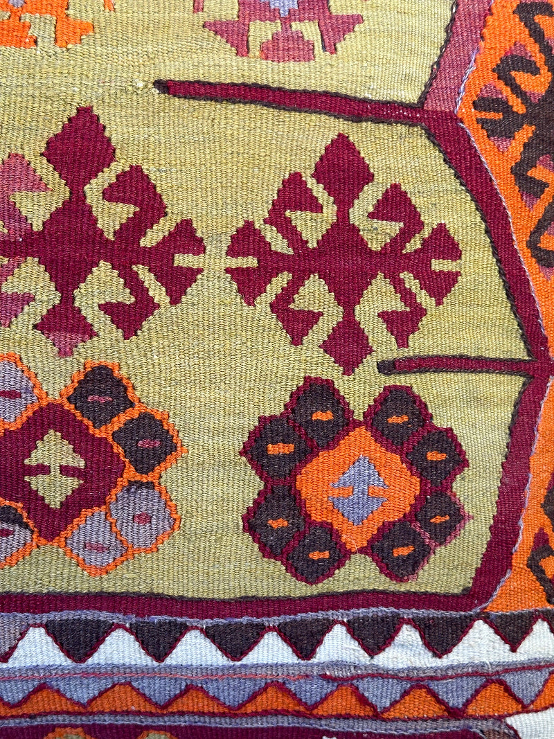 Handwoven kilim pillow crafted from upcycled Turkish rugs, featuring vibrant tribal motifs in olive green, burgundy, orange, and gray tones