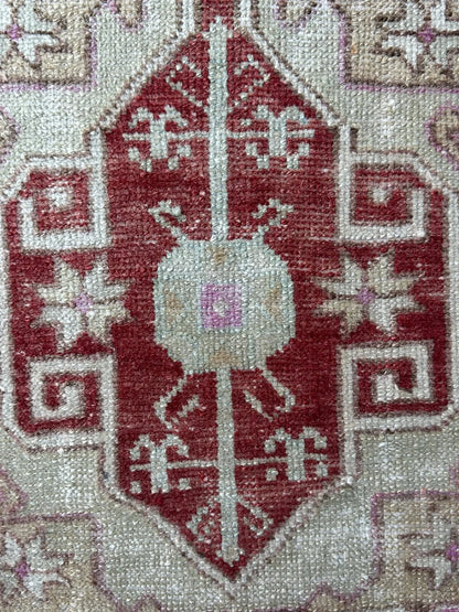 4 by 2 small Turkish area rug featuring deep red hues and light sand and tan coloring with two large medallions in the center bordered by geometric shapes and florals