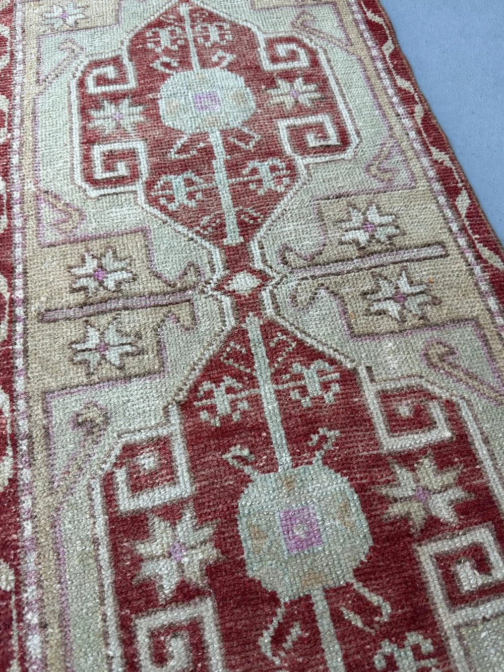 4 by 2 small Turkish area rug featuring deep red hues and light sand and tan coloring with two large medallions in the center bordered by geometric shapes and florals