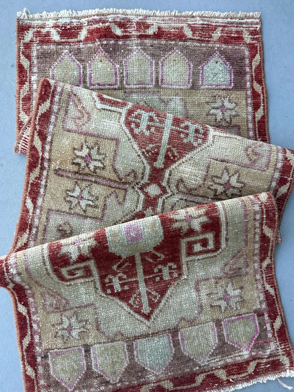 4 by 2 small Turkish area rug featuring deep red hues and light sand and tan coloring with two large medallions in the center bordered by geometric shapes and florals