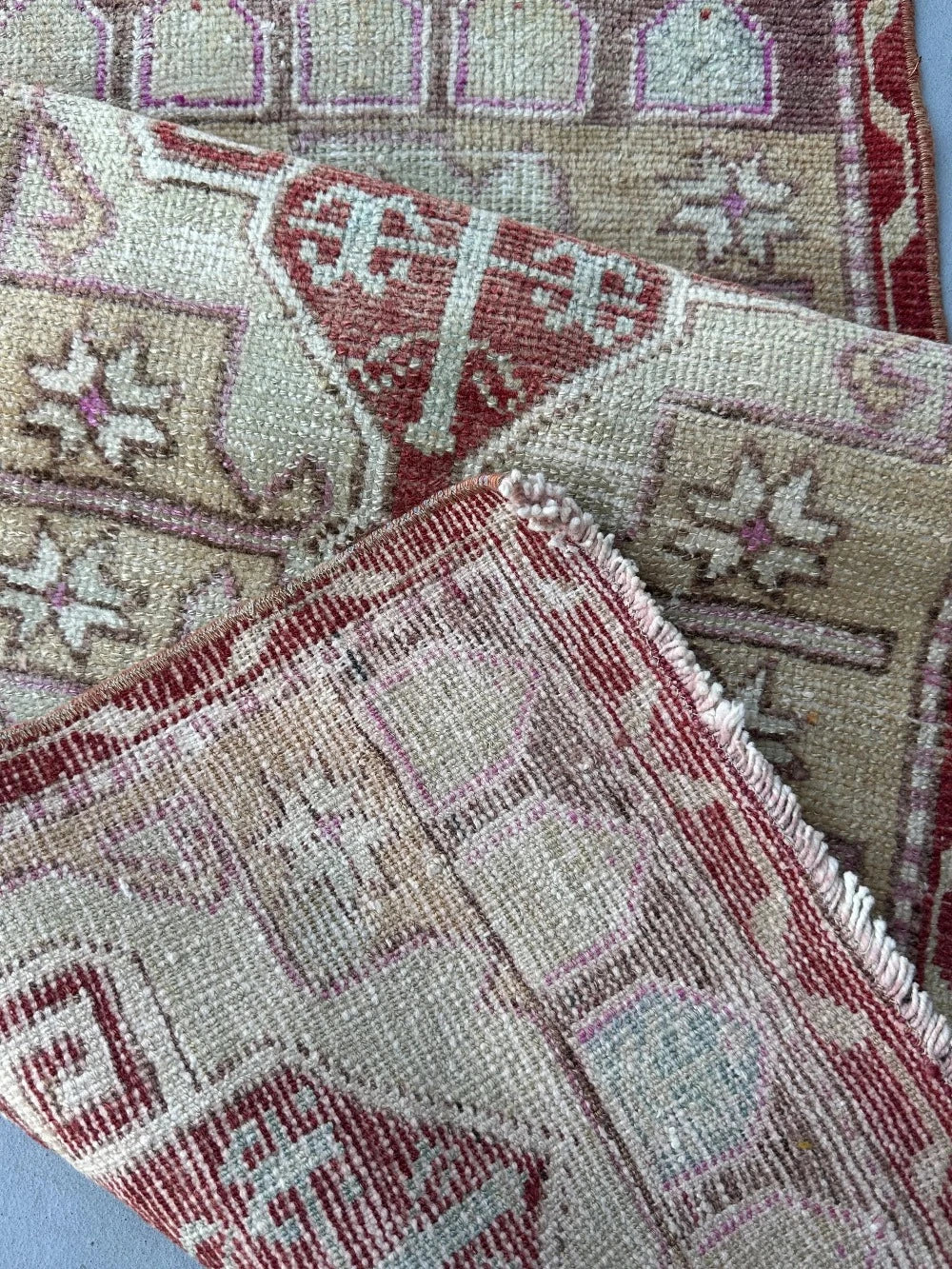 4 by 2 small Turkish area rug featuring deep red hues and light sand and tan coloring with two large medallions in the center bordered by geometric shapes and florals