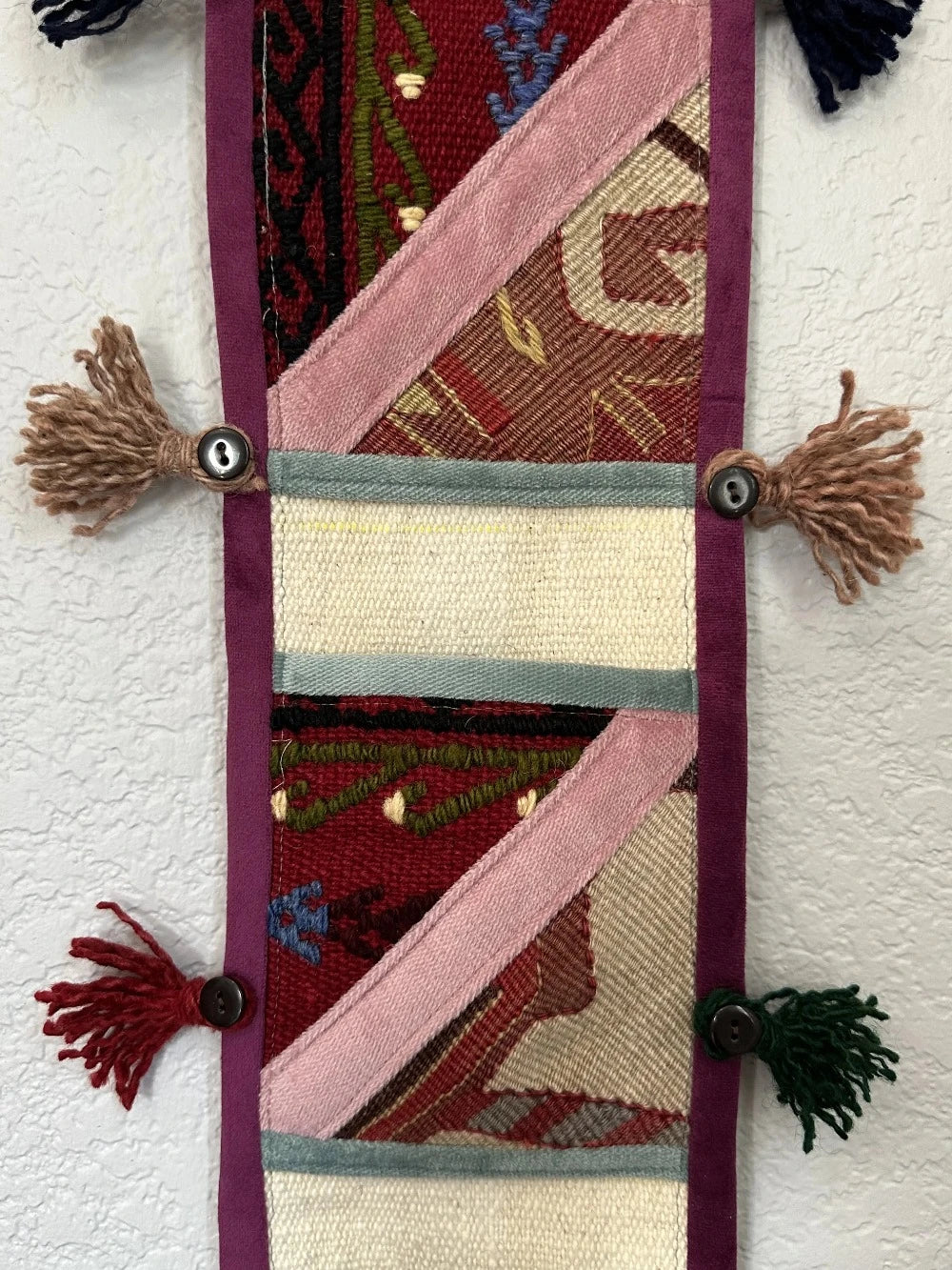 multi-colored three pocket wall organizer made from scraps of colorful Turkish kilim rugs with yarn tassels at each end