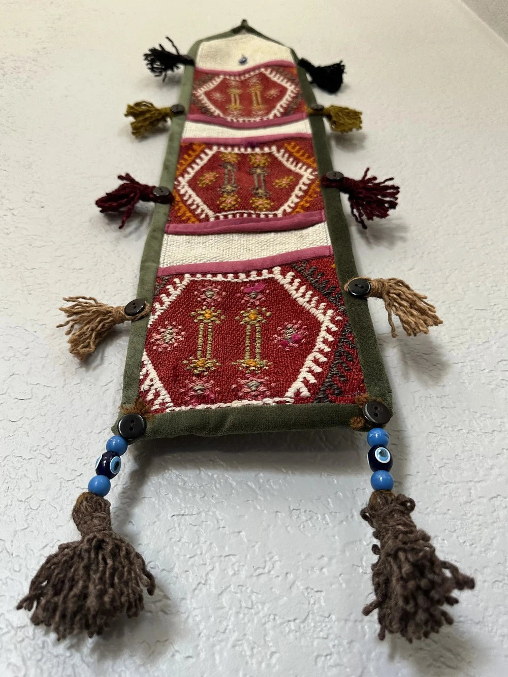 multi-colored three pocket wall organizer made from scraps of colorful Turkish kilim rugs with yarn tassels at each end