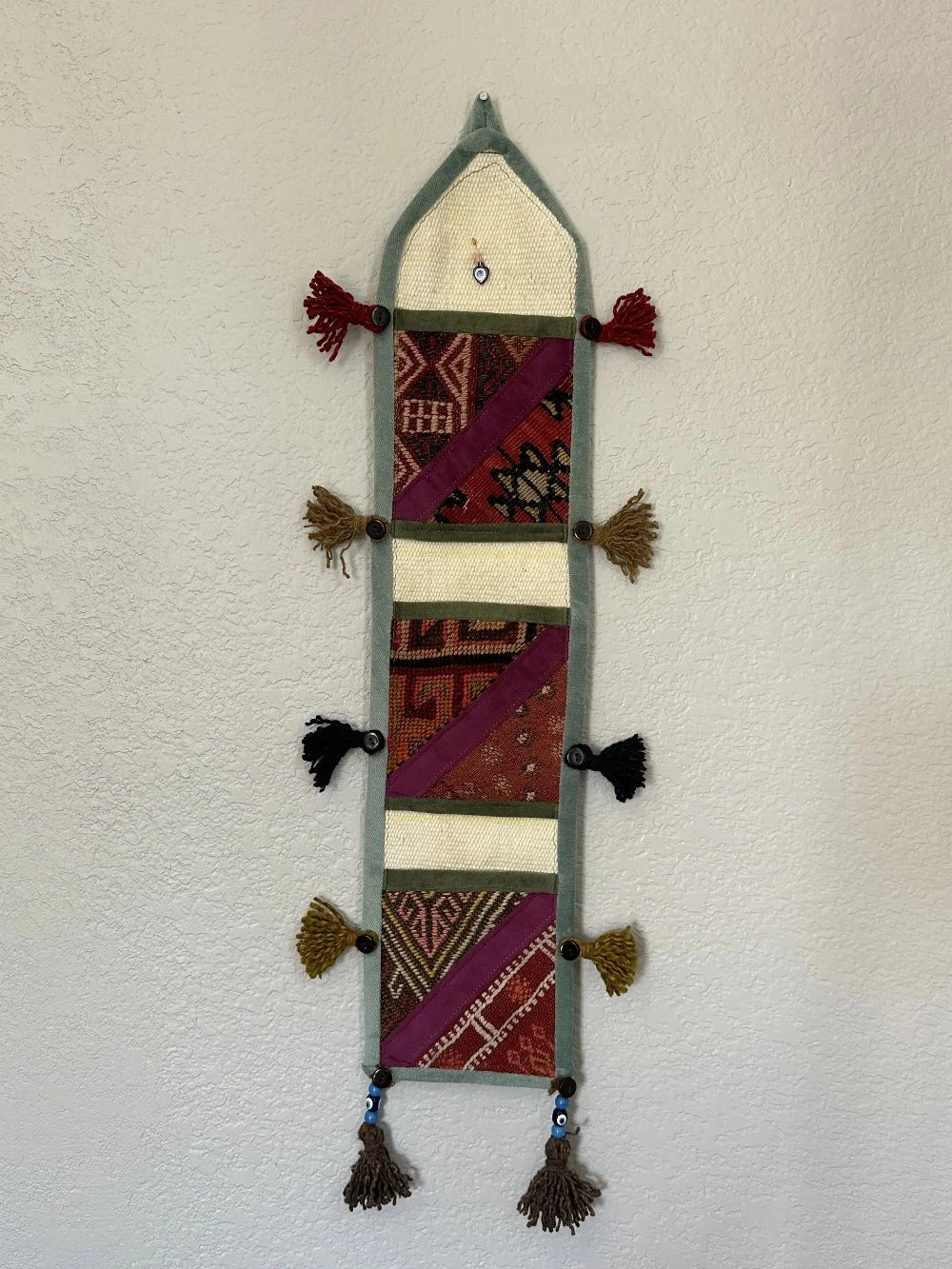 multi-colored three pocket wall organizer made from scraps of colorful Turkish kilim rugs with yarn tassels at each end