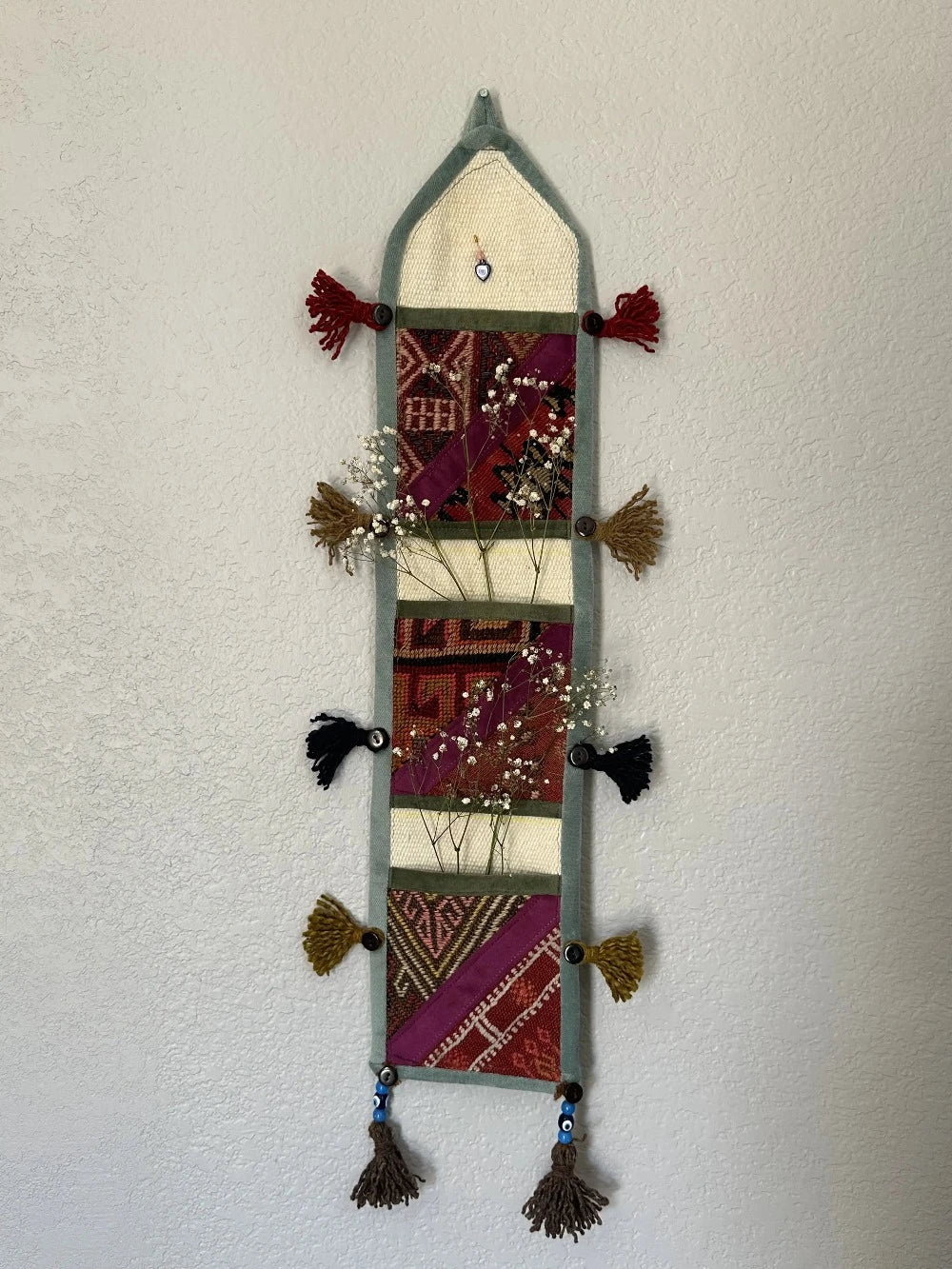 multi-colored three pocket wall organizer made from scraps of colorful Turkish kilim rugs with yarn tassels at each end