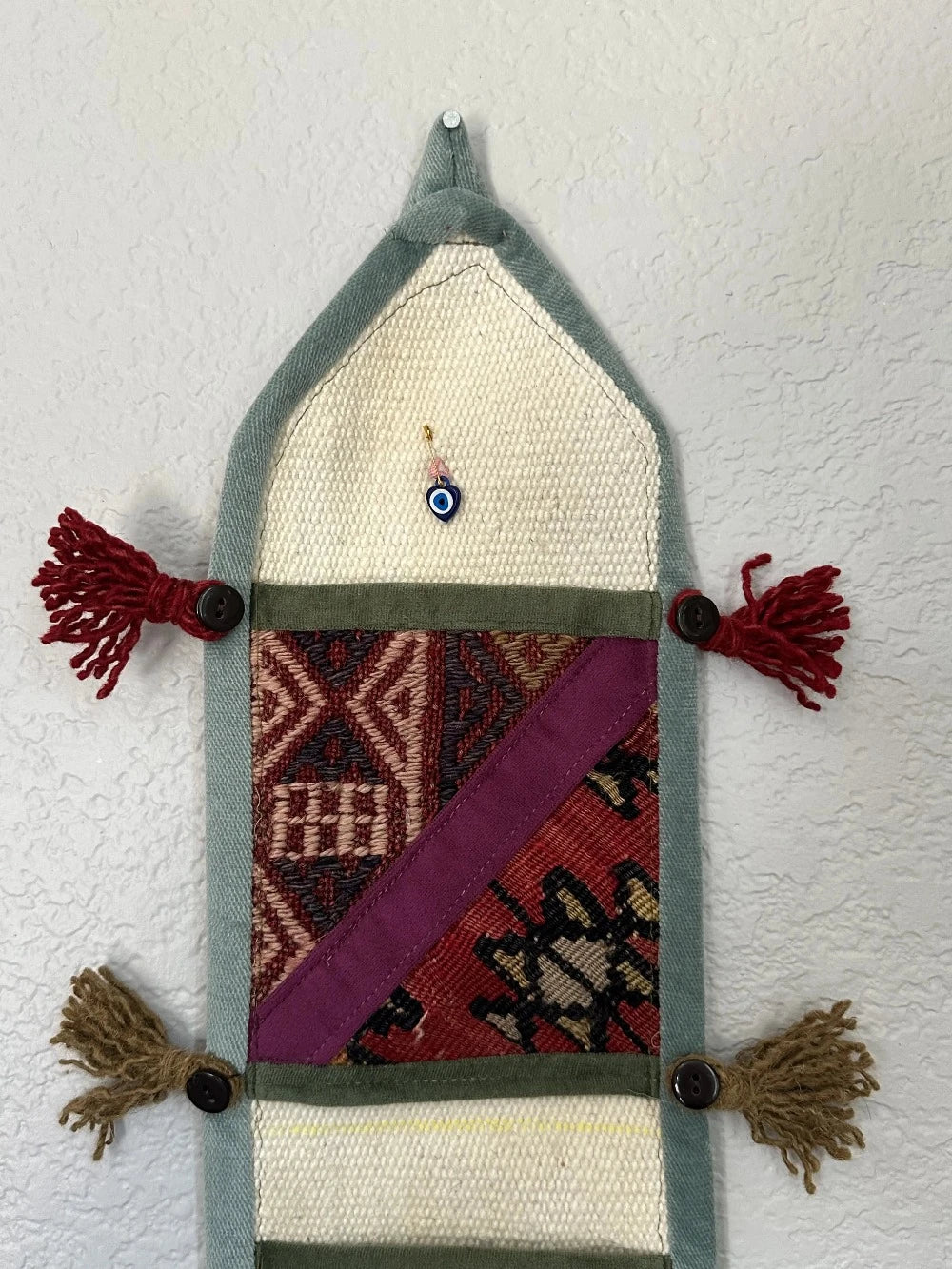 multi-colored three pocket wall organizer made from scraps of colorful Turkish kilim rugs with yarn tassels at each end