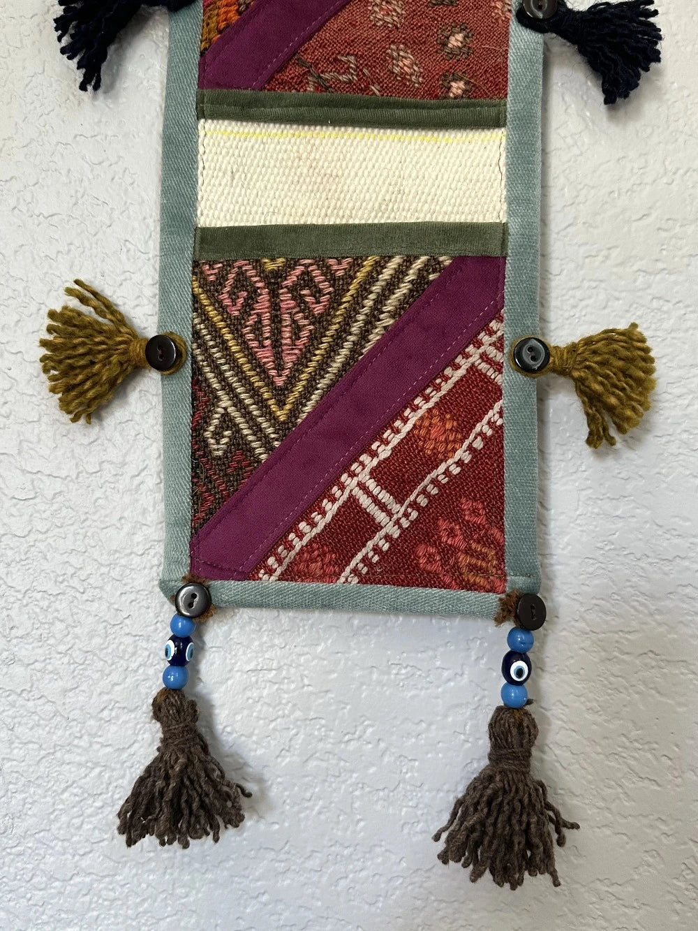 multi-colored three pocket wall organizer made from scraps of colorful Turkish kilim rugs with yarn tassels at each end