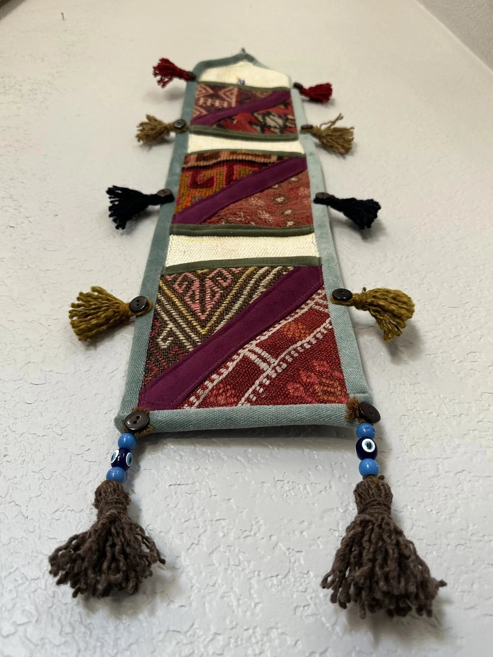 multi-colored three pocket wall organizer made from scraps of colorful Turkish kilim rugs with yarn tassels at each end