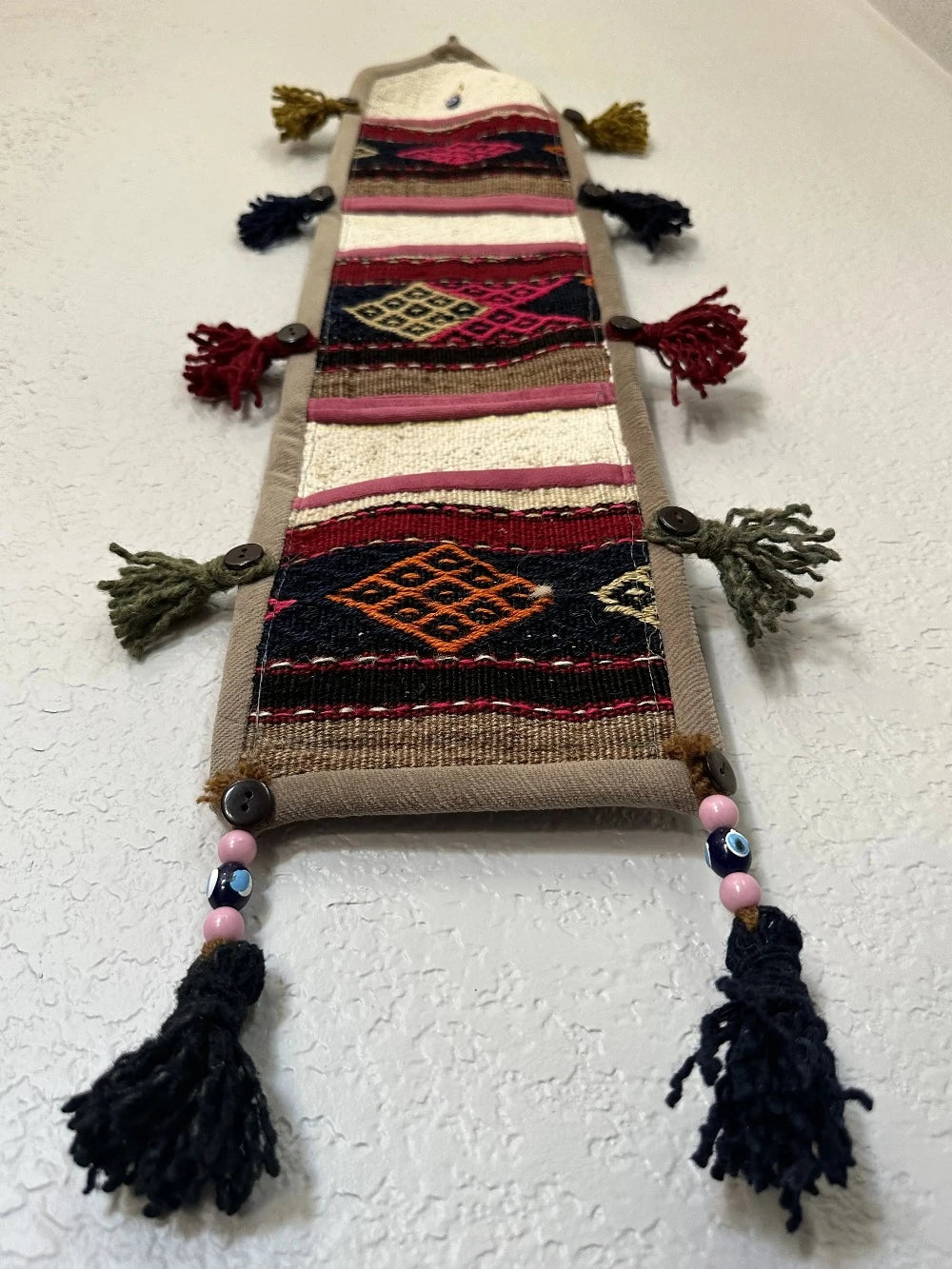 multi-colored three pocket wall organizer made from scraps of colorful Turkish kilim rugs with yarn tassels at each end