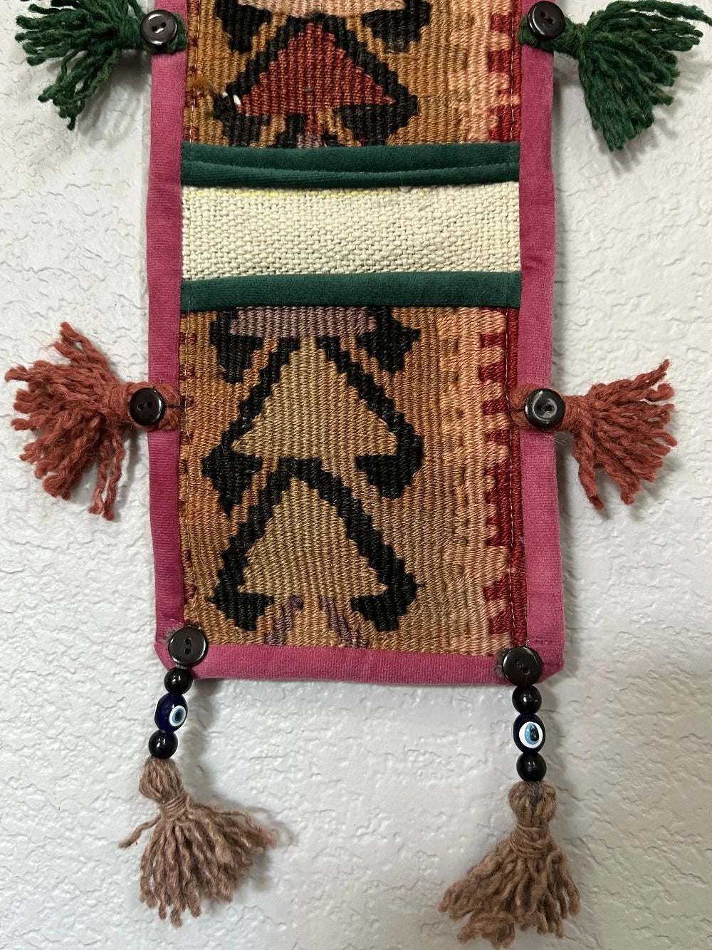 multi-colored three pocket wall organizer made from scraps of colorful Turkish kilim rugs with yarn tassels at each end