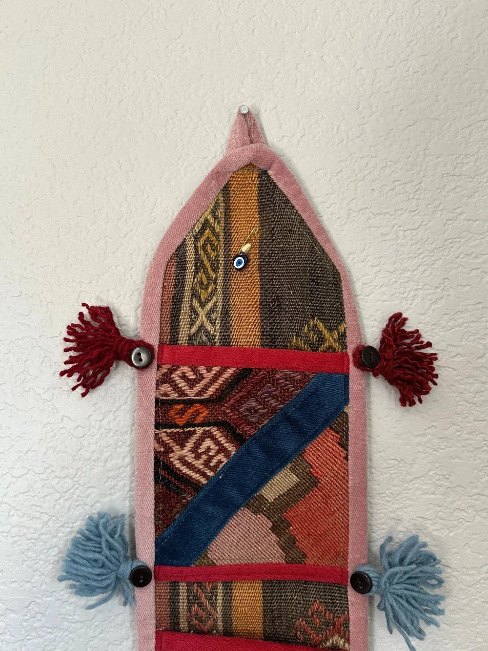 multi-colored three pocket wall organizer made from scraps of colorful Turkish kilim rugs with yarn tassels at each end