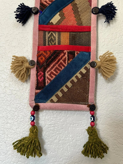 multi-colored three pocket wall organizer made from scraps of colorful Turkish kilim rugs with yarn tassels at each end