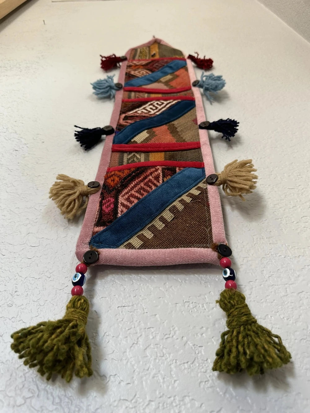 multi-colored three pocket wall organizer made from scraps of colorful Turkish kilim rugs with yarn tassels at each end