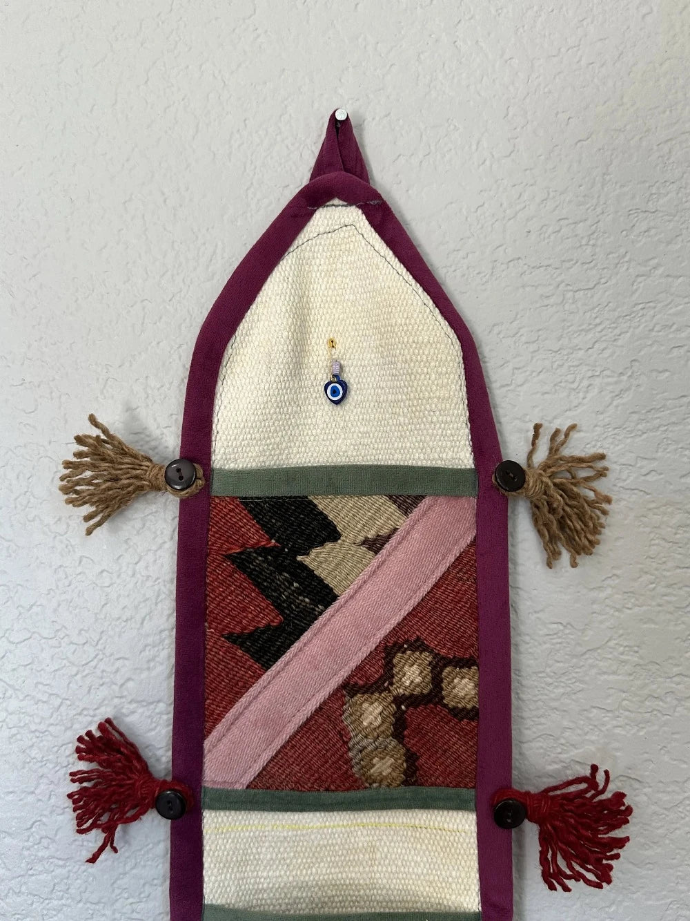 multi-colored three pocket wall organizer made from scraps of colorful Turkish kilim rugs with yarn tassels at each end