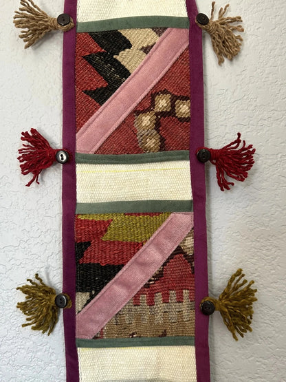 multi-colored three pocket wall organizer made from scraps of colorful Turkish kilim rugs with yarn tassels at each end