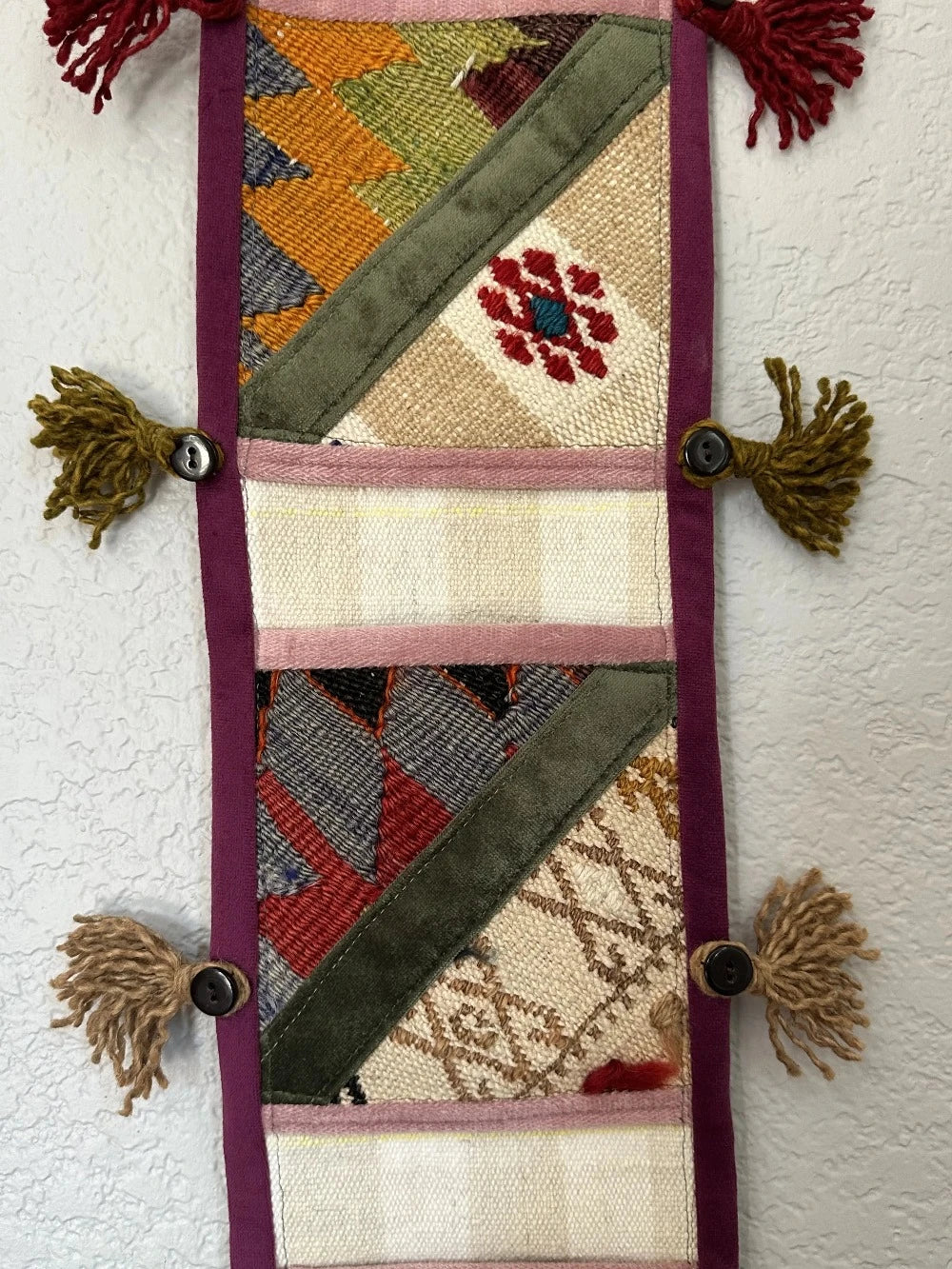 multi-colored three pocket wall organizer made from scraps of colorful Turkish kilim rugs with yarn tassels at each end