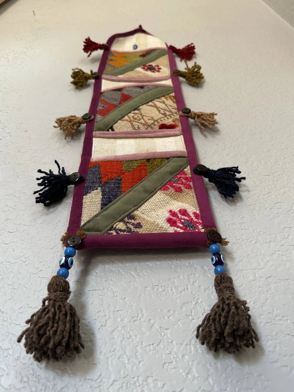 multi-colored three pocket wall organizer made from scraps of colorful Turkish kilim rugs with yarn tassels at each end