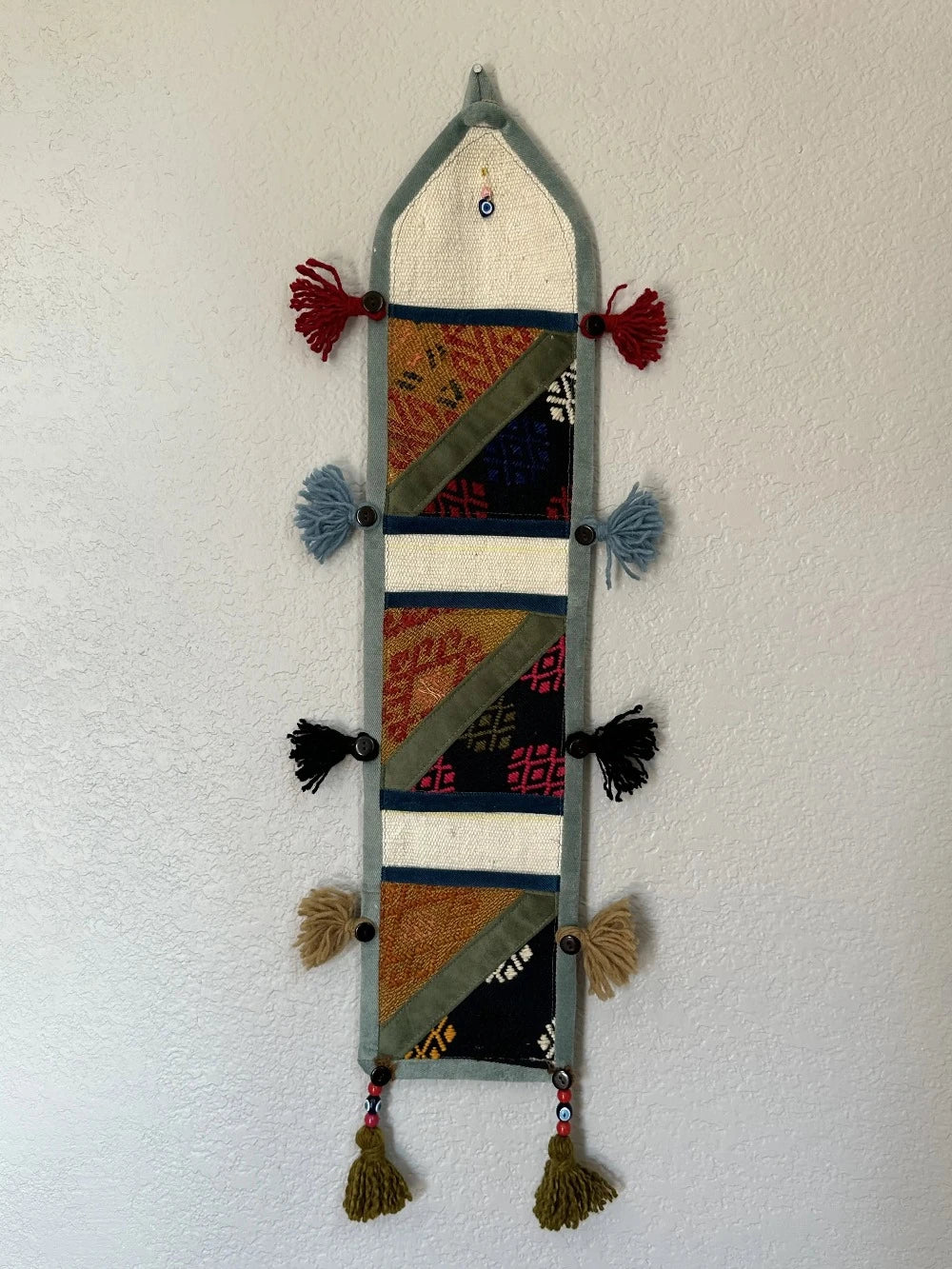 multi-colored three pocket wall organizer made from scraps of colorful Turkish kilim rugs with yarn tassels at each end