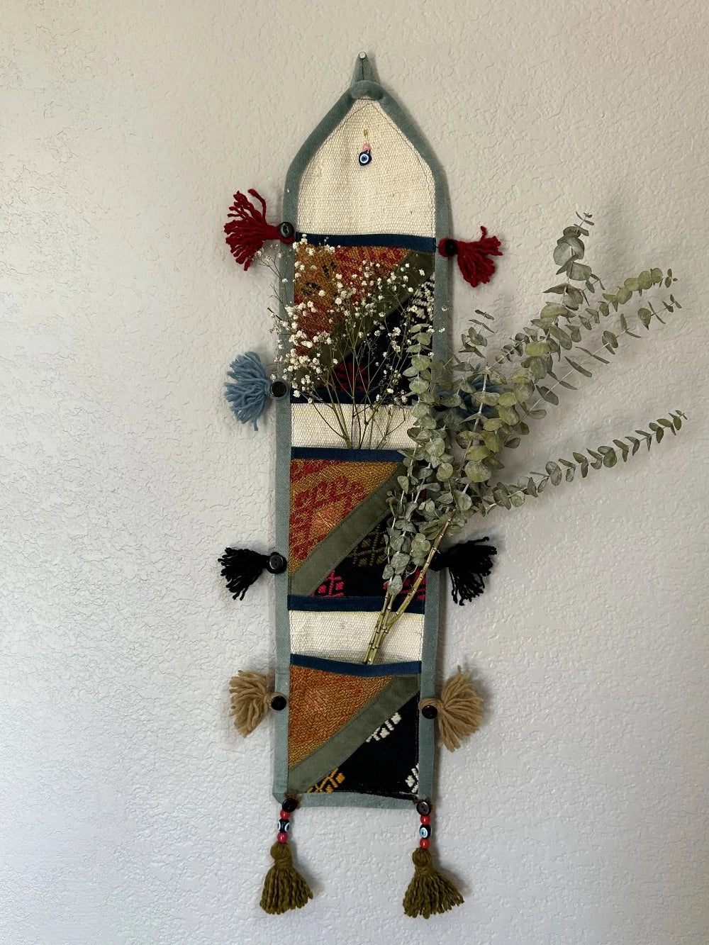 multi-colored three pocket wall organizer made from scraps of colorful Turkish kilim rugs with yarn tassels at each end