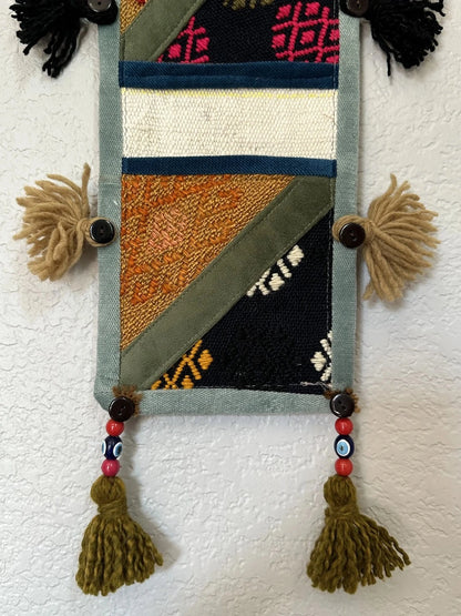 multi-colored three pocket wall organizer made from scraps of colorful Turkish kilim rugs with yarn tassels at each end