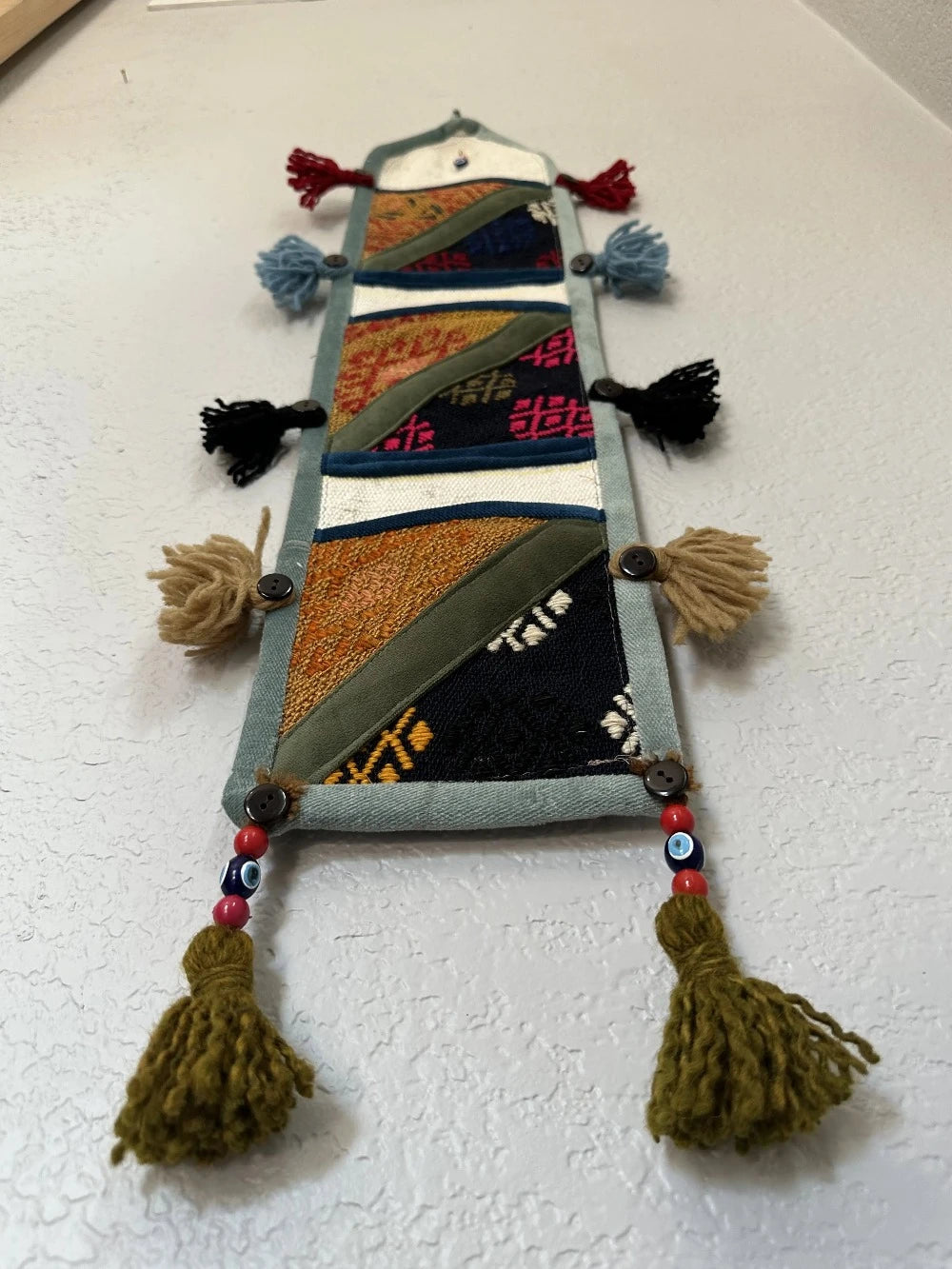 multi-colored three pocket wall organizer made from scraps of colorful Turkish kilim rugs with yarn tassels at each end