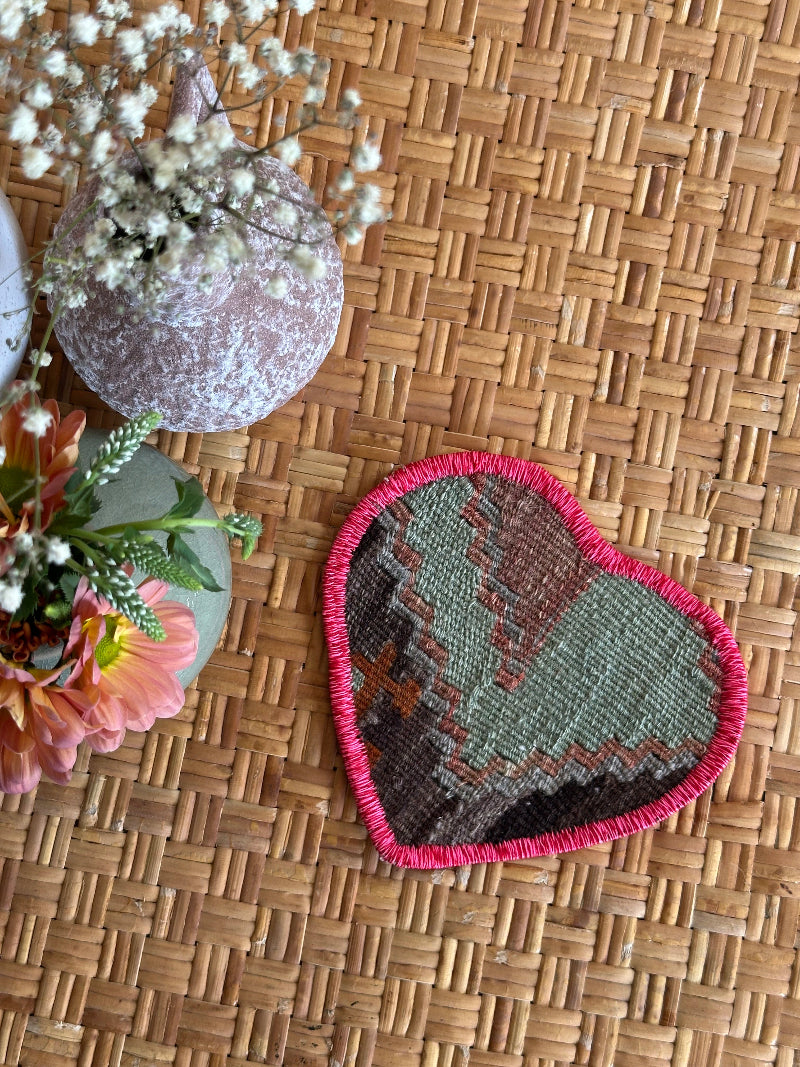 six inch heart-shaped Turkish rug hot plate made from repurposed vintage rugs with light green and brown tones and embroidered trim, perfect for hot pans, plants, or decor.
