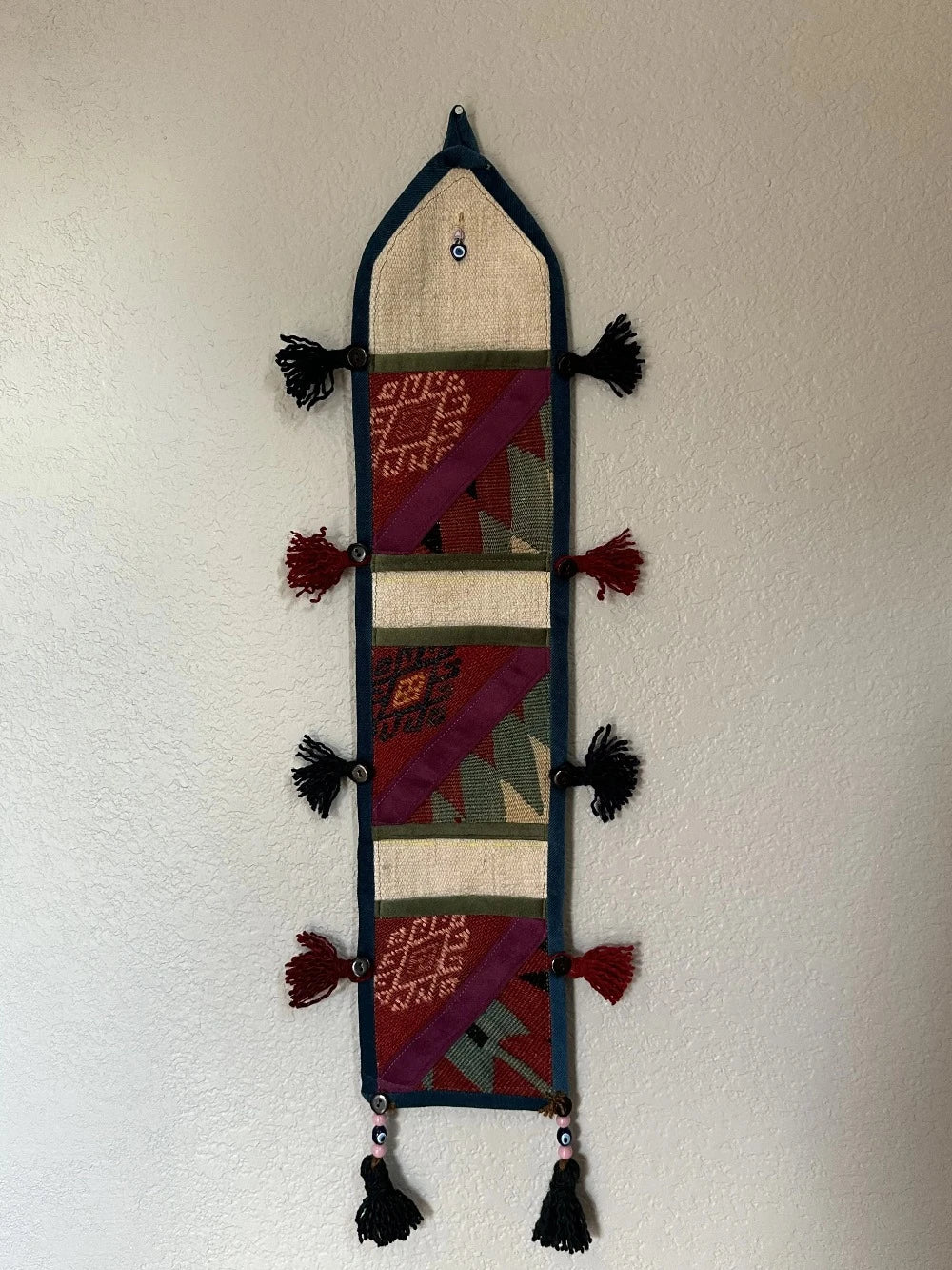 multi-colored three pocket wall organizer made from scraps of colorful Turkish kilim rugs with yarn tassels at each end