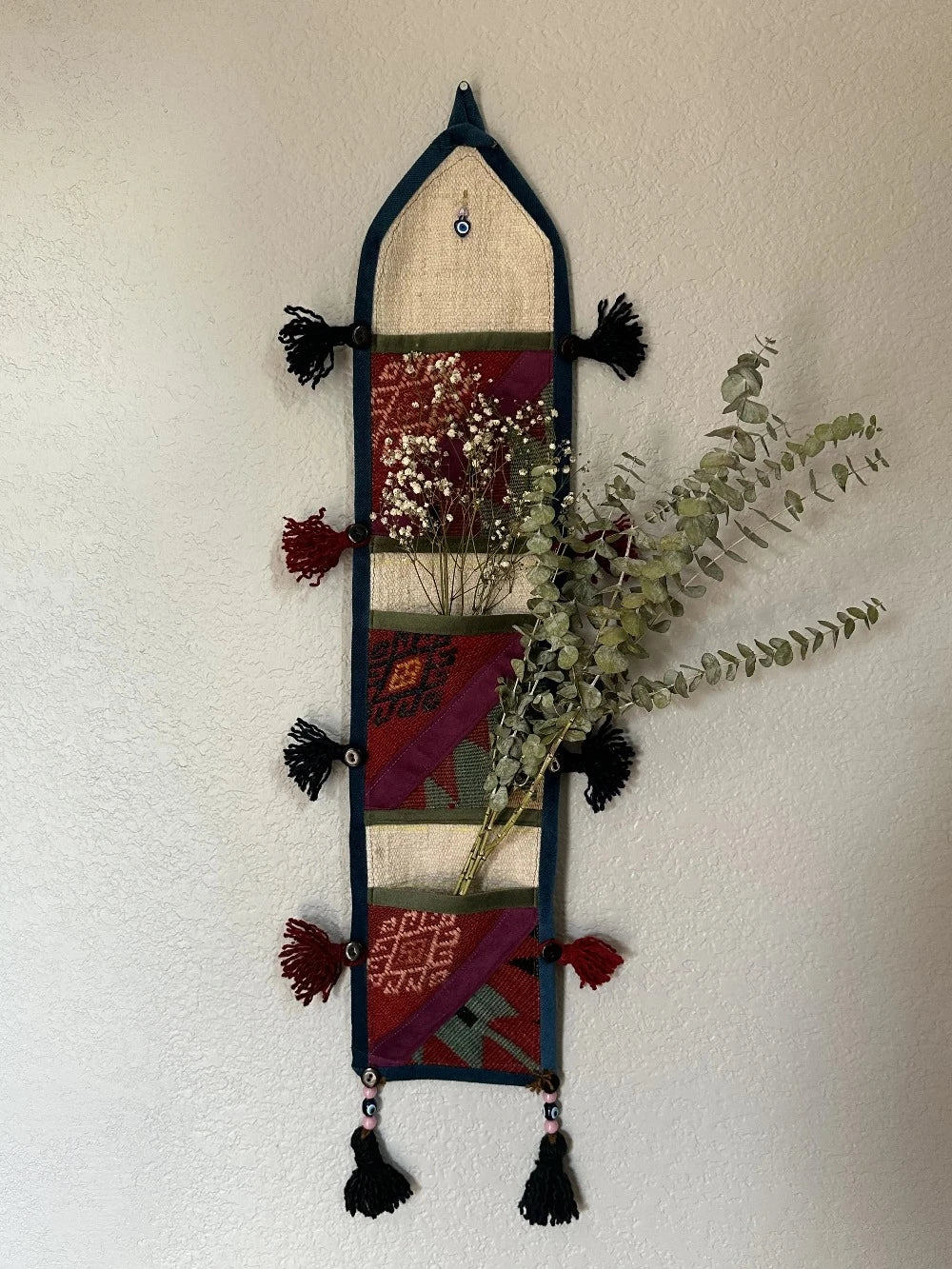 multi-colored three pocket wall organizer made from scraps of colorful Turkish kilim rugs with yarn tassels at each end