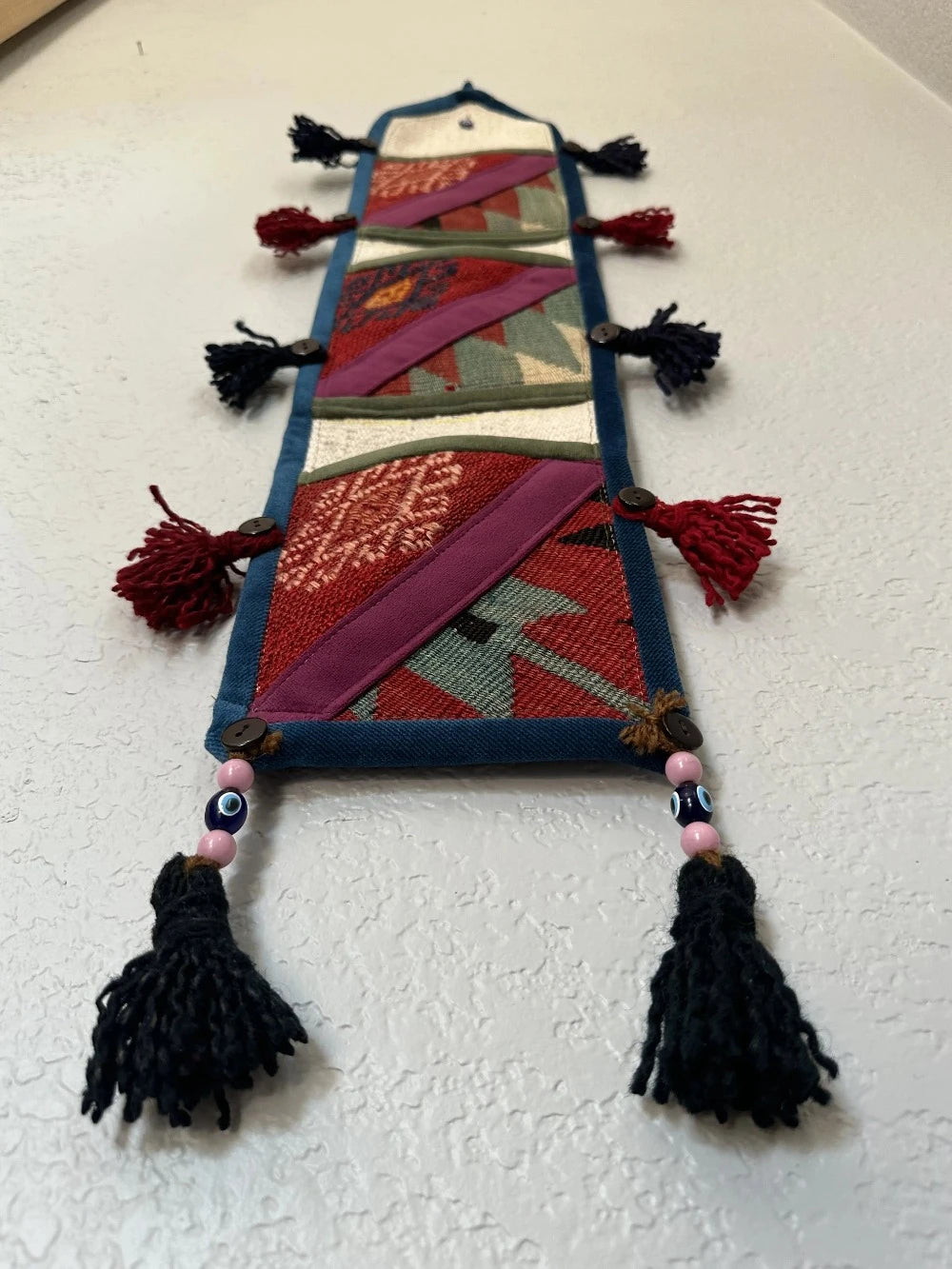 multi-colored three pocket wall organizer made from scraps of colorful Turkish kilim rugs with yarn tassels at each end