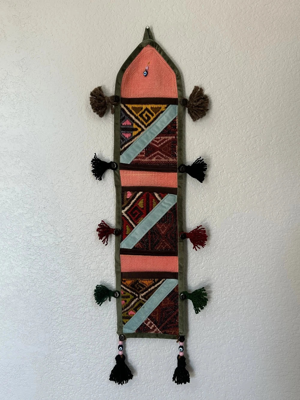 multi-colored three pocket wall organizer made from scraps of colorful Turkish kilim rugs with yarn tassels at each end