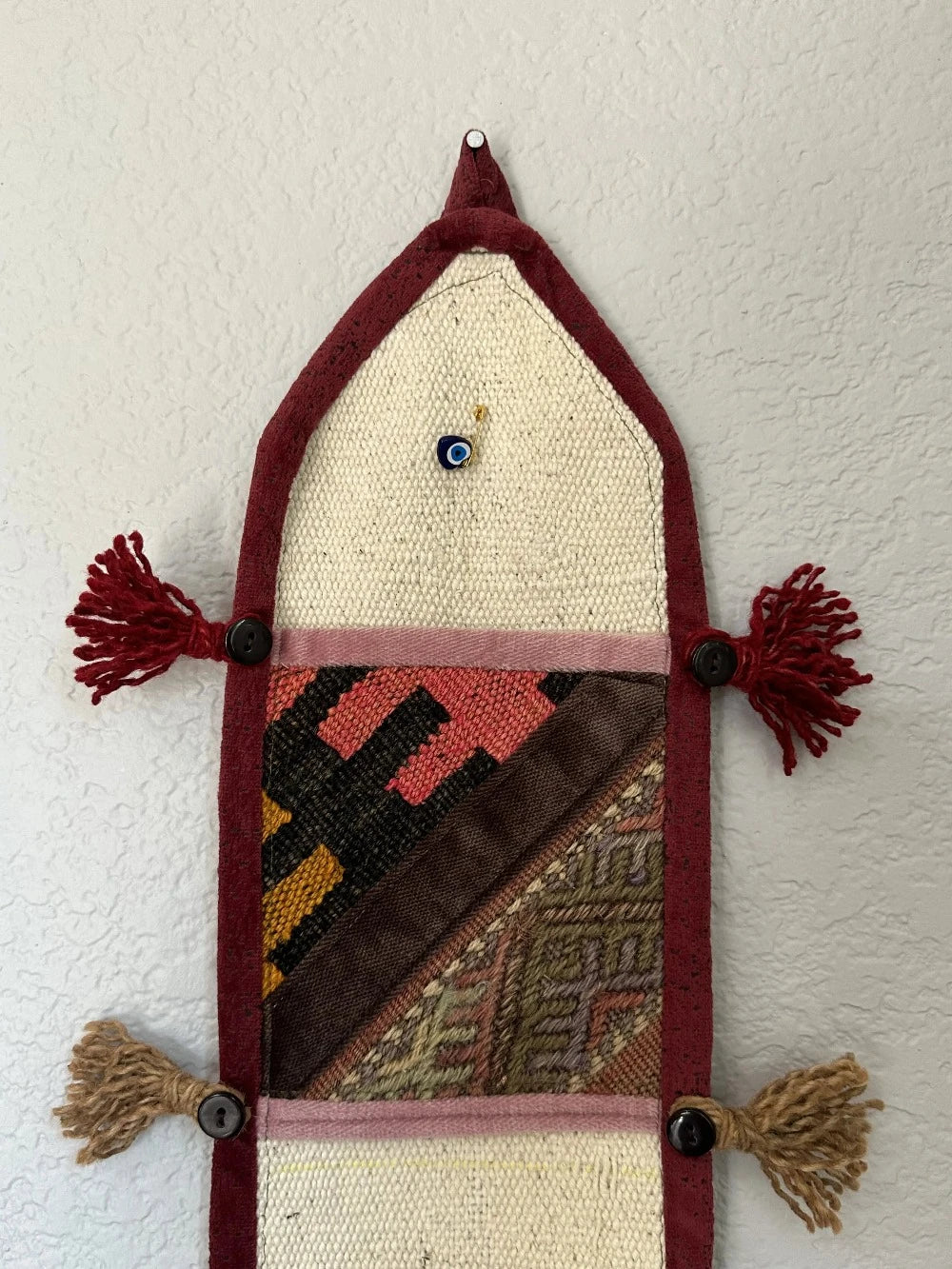 multi-colored three pocket wall organizer made from scraps of colorful Turkish kilim rugs with yarn tassels at each end