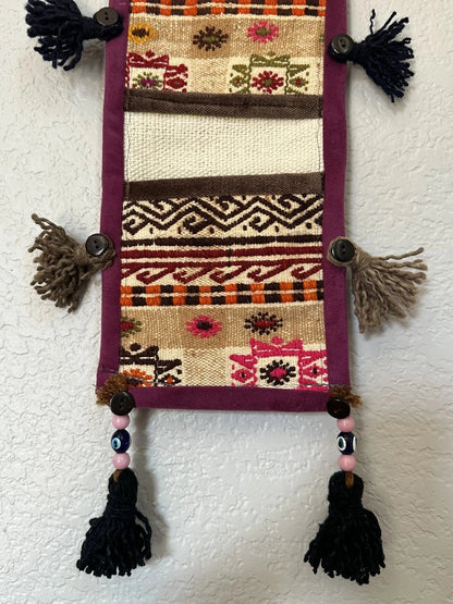 multi-colored three pocket wall organizer made from scraps of colorful Turkish kilim rugs with yarn tassels at each end