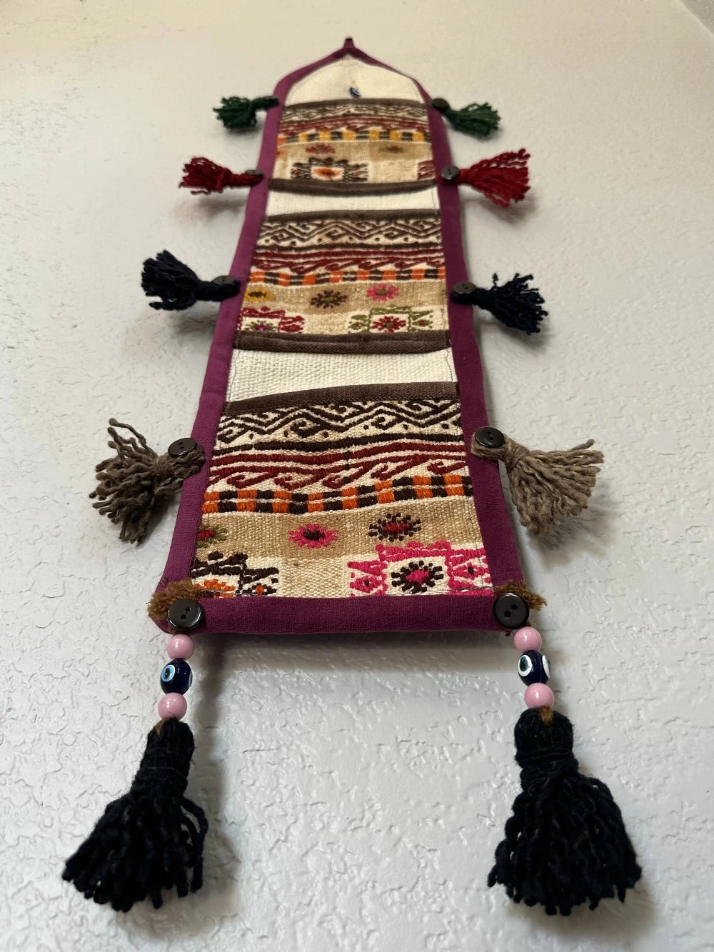 multi-colored three pocket wall organizer made from scraps of colorful Turkish kilim rugs with yarn tassels at each end