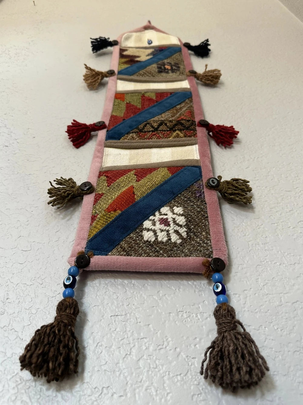 multi-colored three pocket wall organizer made from scraps of colorful Turkish kilim rugs with yarn tassels at each end