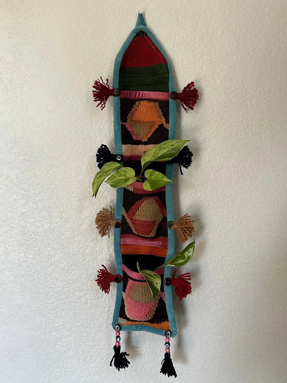 multi-colored three pocket wall organizer made from scraps of colorful Turkish kilim rugs with yarn tassels at each end