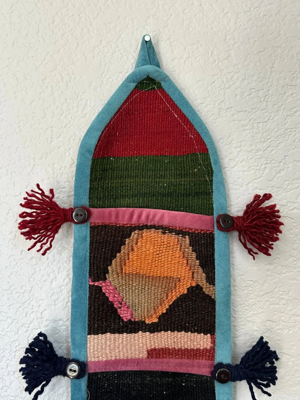 multi-colored three pocket wall organizer made from scraps of colorful Turkish kilim rugs with yarn tassels at each end