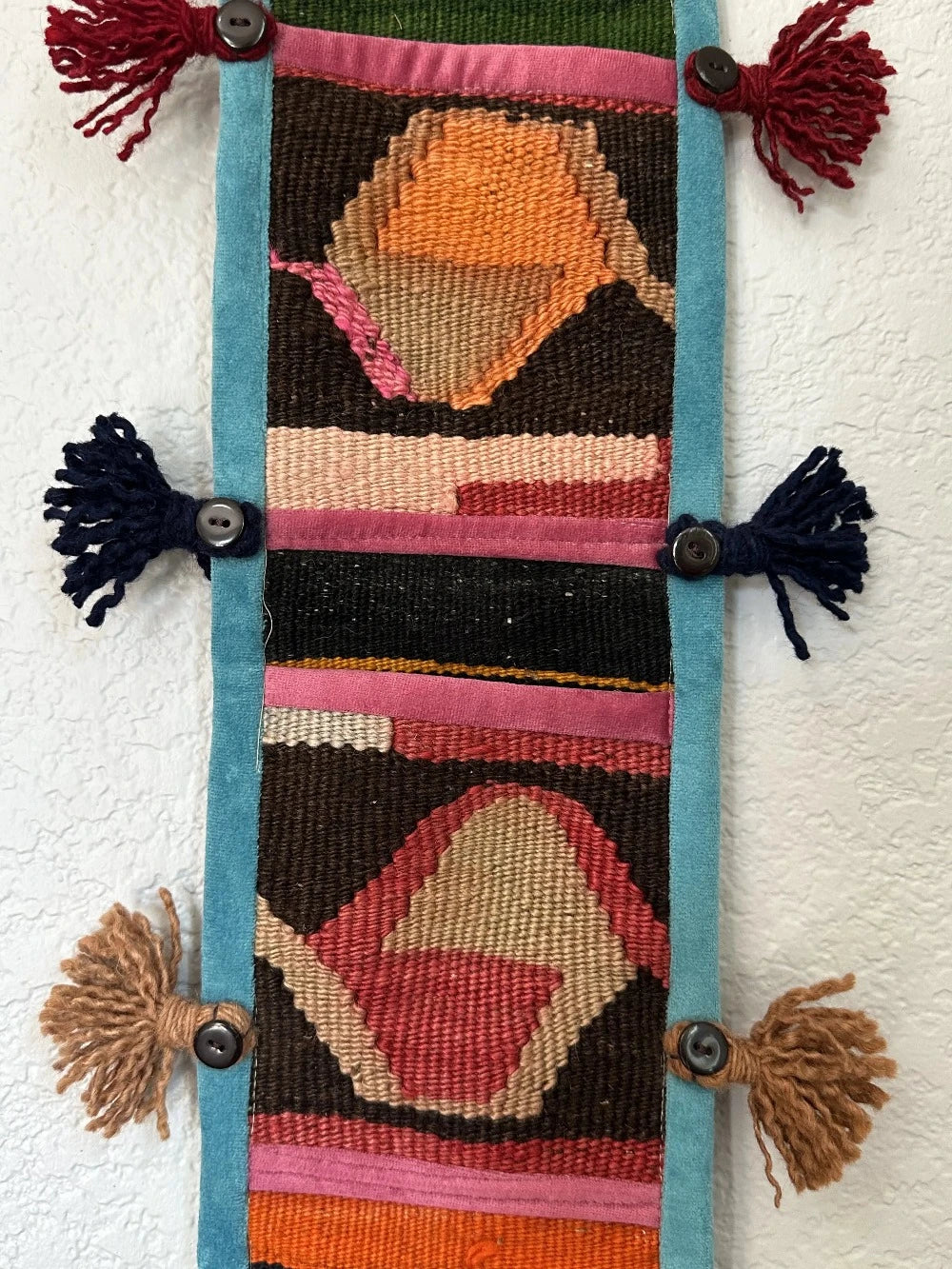 multi-colored three pocket wall organizer made from scraps of colorful Turkish kilim rugs with yarn tassels at each end