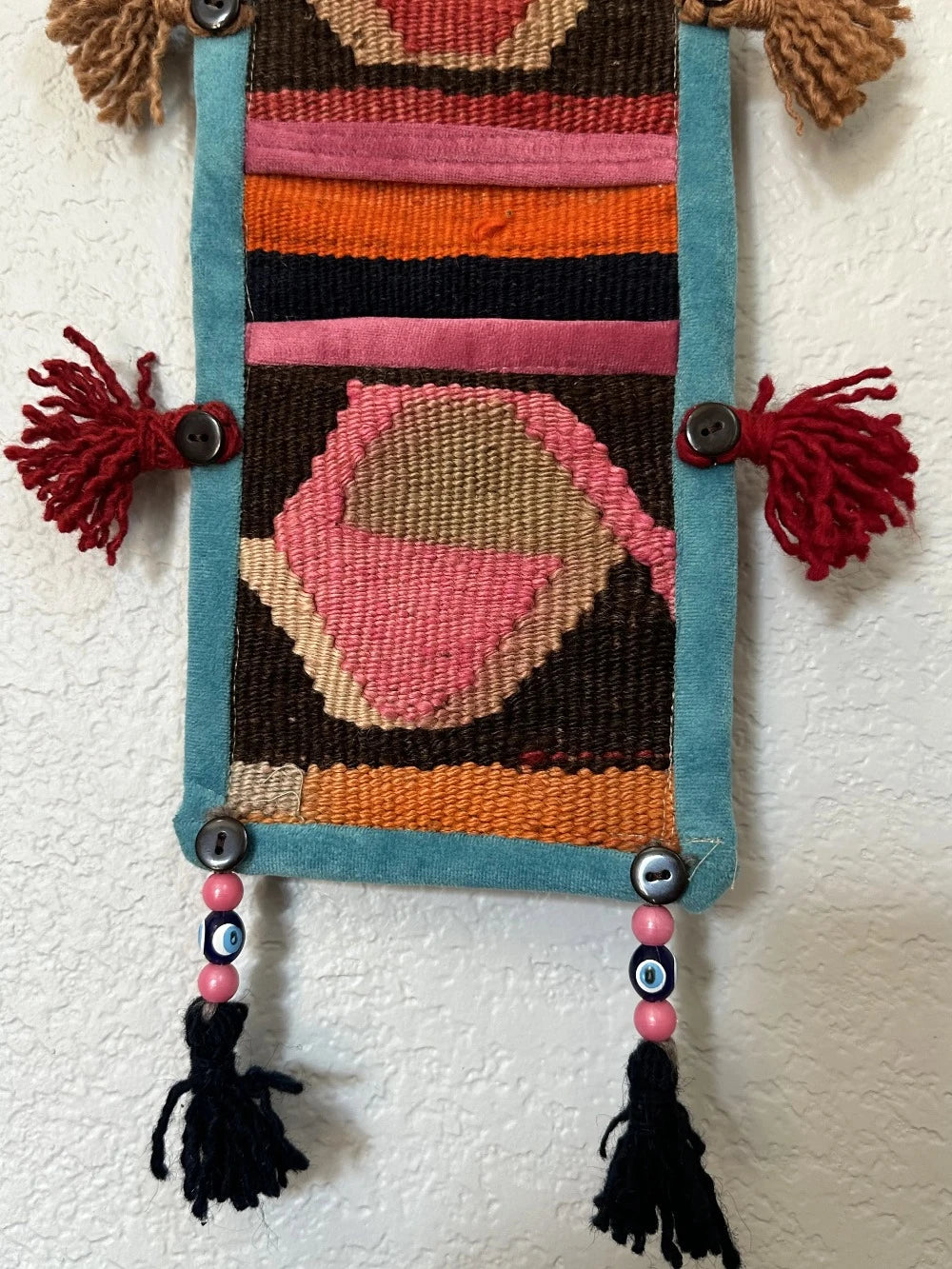 multi-colored three pocket wall organizer made from scraps of colorful Turkish kilim rugs with yarn tassels at each end