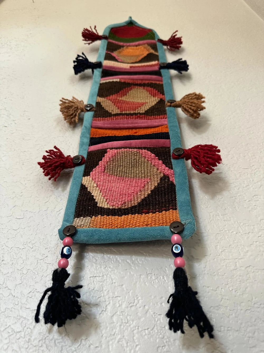 multi-colored three pocket wall organizer made from scraps of colorful Turkish kilim rugs with yarn tassels at each end