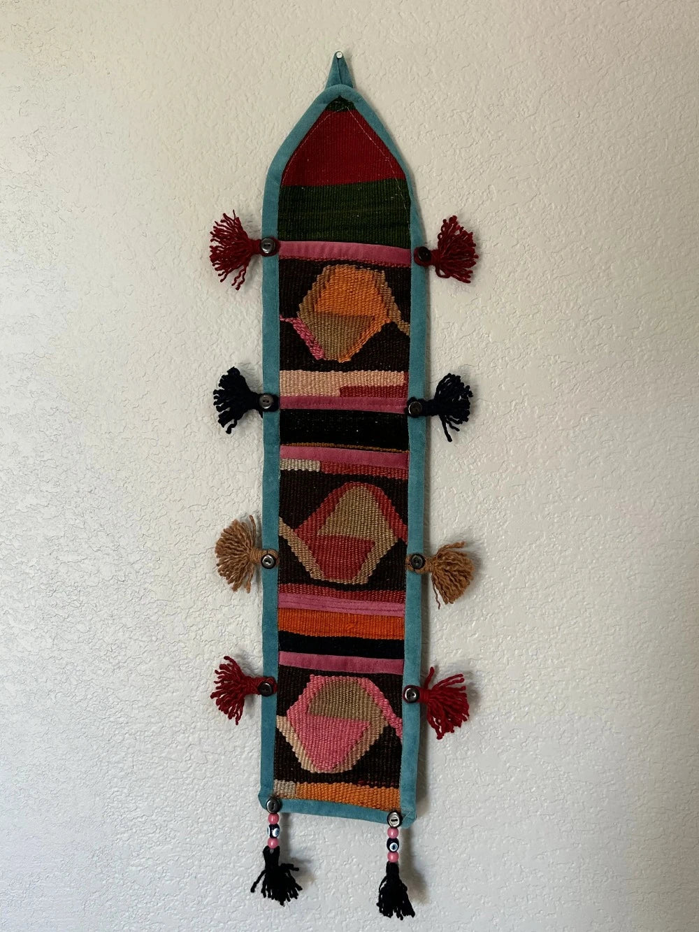 multi-colored three pocket wall organizer made from scraps of colorful Turkish kilim rugs with yarn tassels at each end