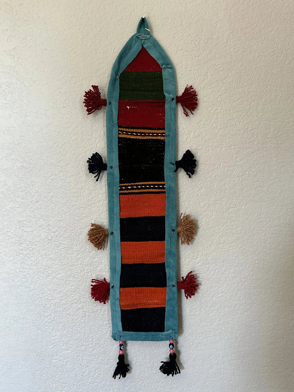 multi-colored three pocket wall organizer made from scraps of colorful Turkish kilim rugs with yarn tassels at each end