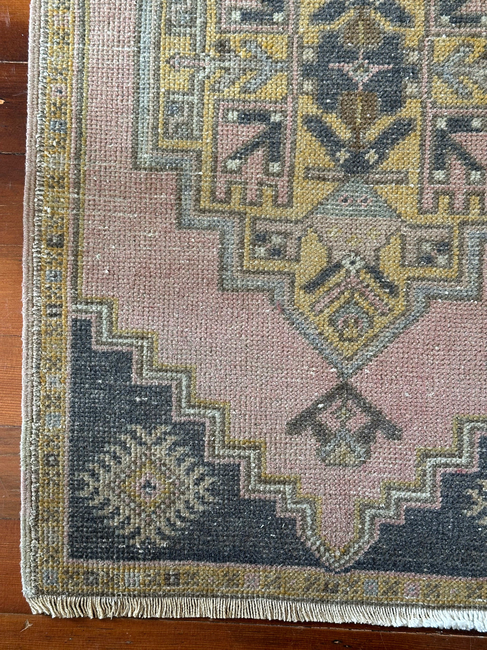 Vintage Turkish wool rug with a central geometric medallion in muted pink, gold, and dark charcoal tones, featuring stepped corner motifs and a distressed finish.